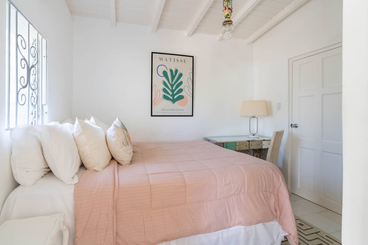 White bedroom with a shell-pink bed and botanical print